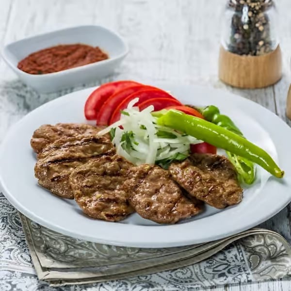 Grilled Turkish meatballs (kofte) with sliced tomatoes, onions, and green peppers on a white plate.
